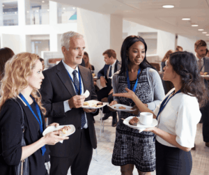 Four professionals conversing and holding plates of food at a networking event.