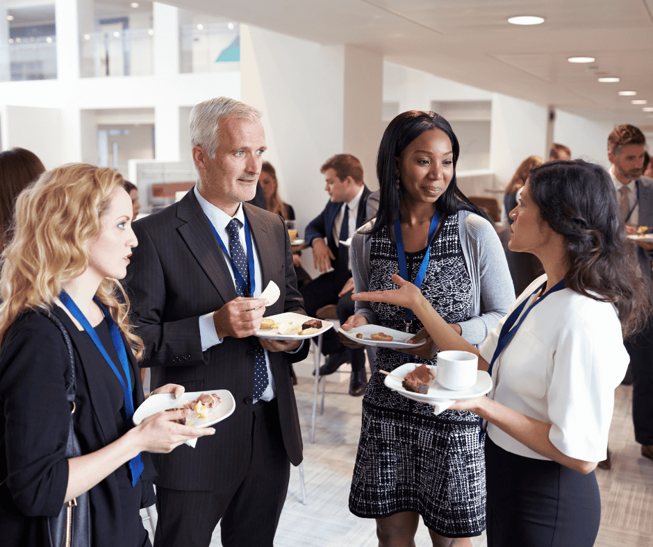 Four professionals conversing and holding plates of food at a networking event.