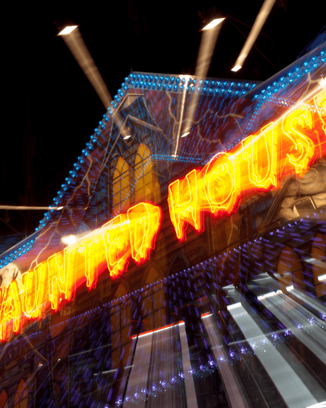 Neon sign reading “Haunted House” glowing in red and yellow lights with motion blur effects, creating a spooky, energetic vibe at night.
