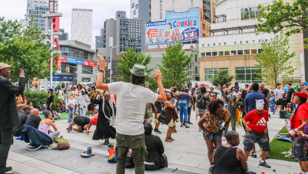 Crowd gathered at the Plaza at 300 Ashland in Downtown Brooklyn during a community event, with people dancing, socializing, and enjoying the open public space surrounded by modern buildings.