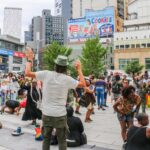 Crowd gathered at the Plaza at 300 Ashland in Downtown Brooklyn during a community event, with people dancing, socializing, and enjoying the open public space surrounded by modern buildings.