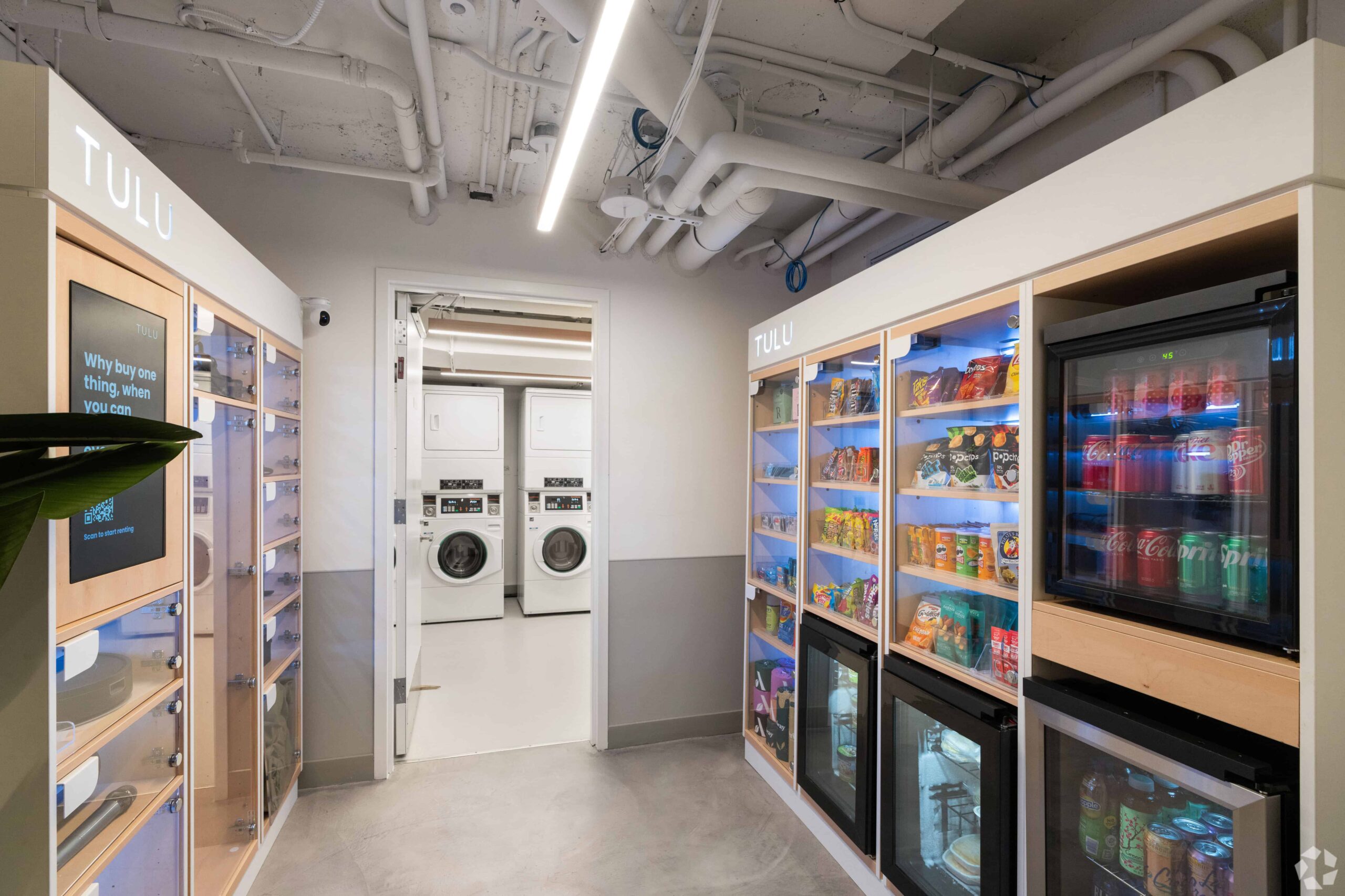 TULU smart vending machines at Webster Apartments stocked with drinks and snacks, located next to the laundry room with washers and dryers in view.
