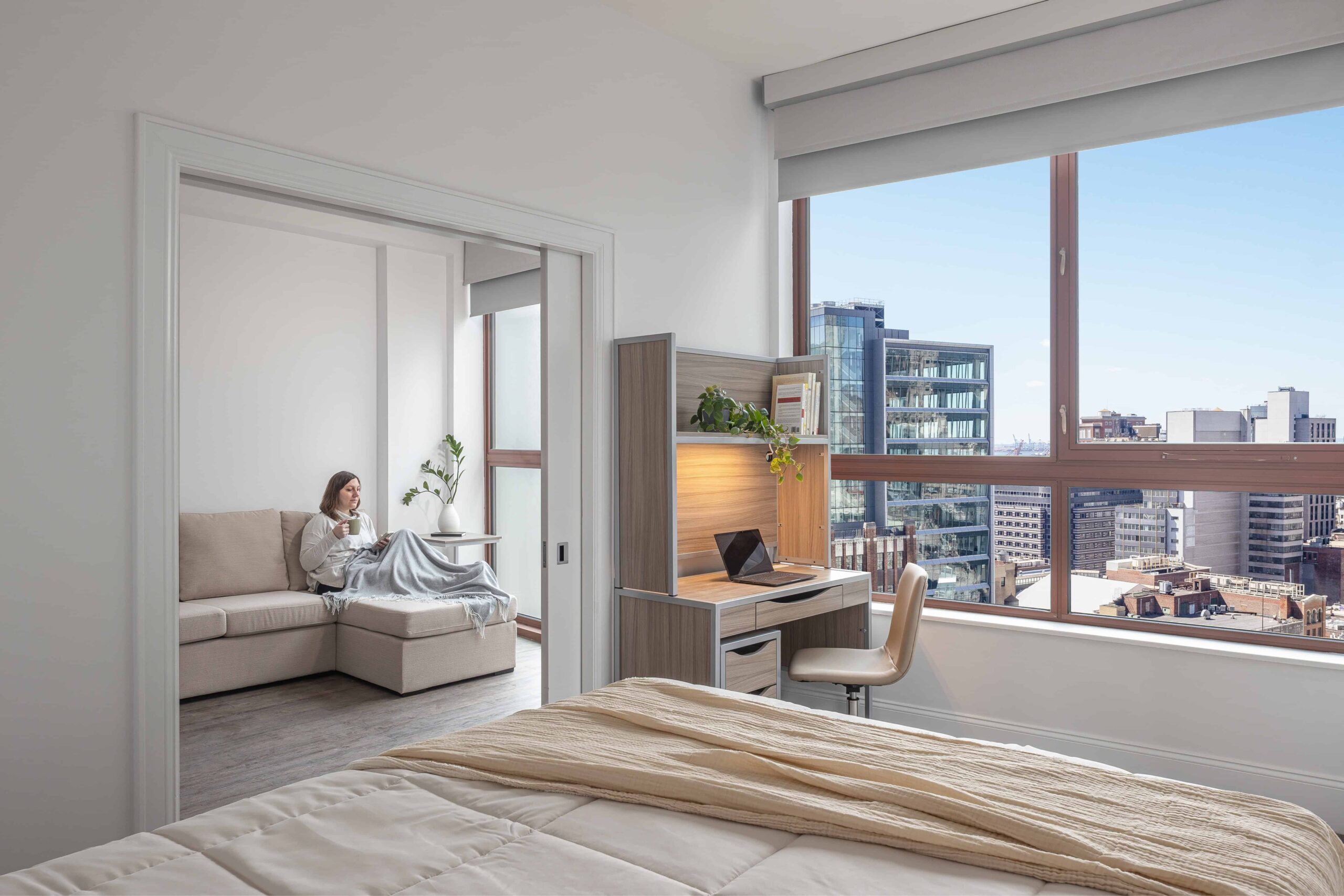 Fully furnished apartment at Webster Apartments in Downtown Brooklyn, featuring a comfortable living space with a view, a cozy seating area, and a desk perfect for young women living in NYC.