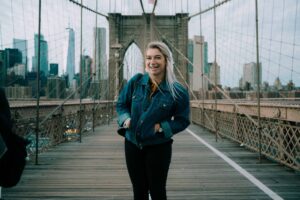 A person smiling on the Brooklyn Bridge with the New York City skyline in the background.